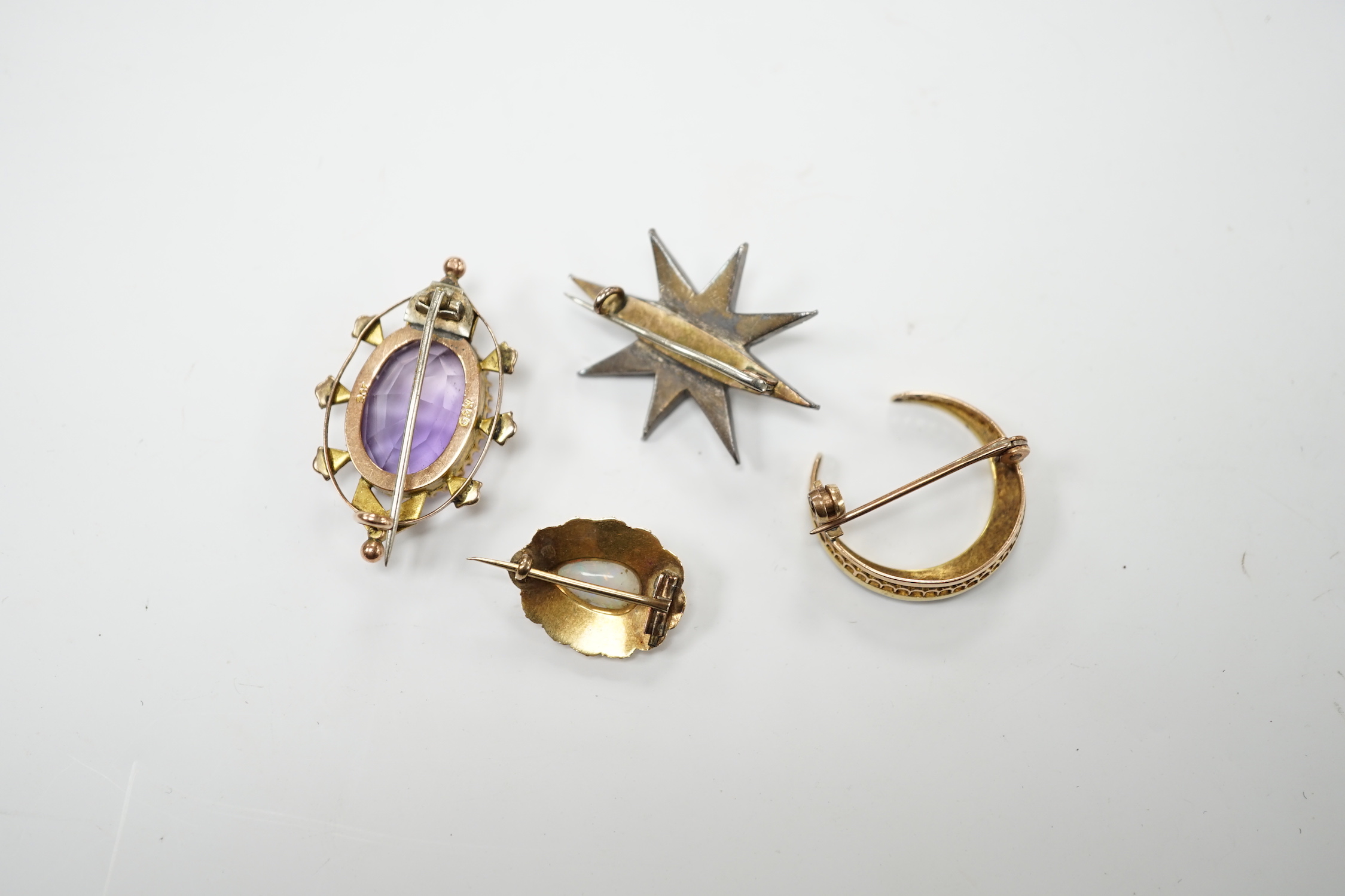 An early 20th century 9ct, amethyst and seed pearl set oval brooch, 33mm, a yellow metal and seed pearl set crescent brooch, a yellow metal, opal and split pearl set brooch and a rose cut diamond and split pearl set star